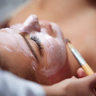 A close-up of a person's upper body being painted with a brush, showcasing artistic body painting techniques in a soft-focus environment.